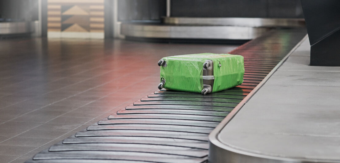 Ein in grüner Folie eingewickelter Koffer auf einem Gepäckband.