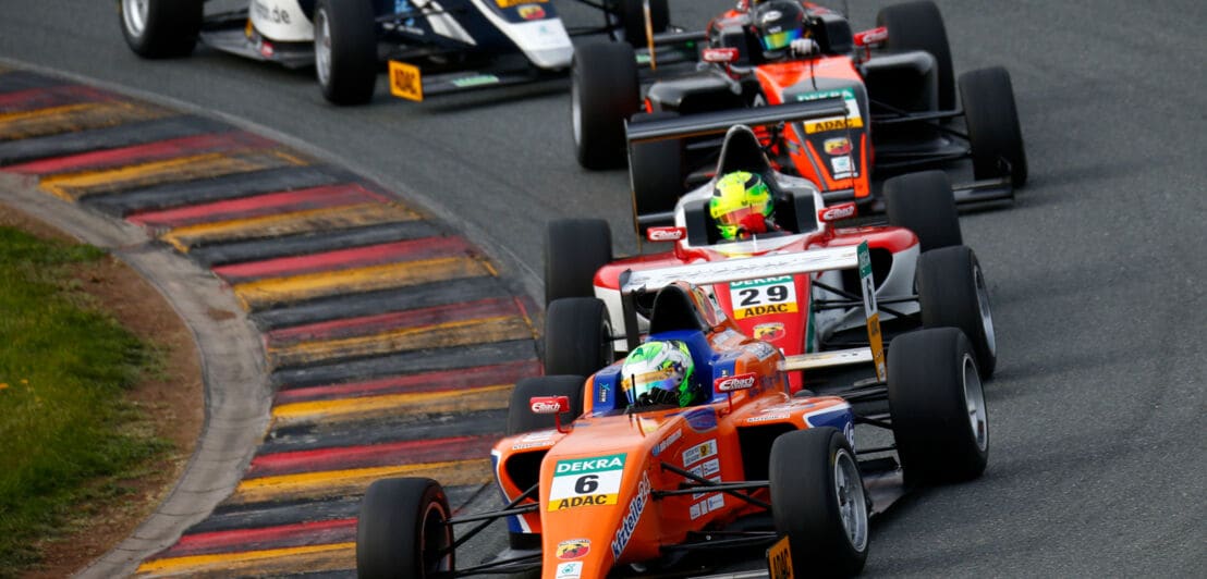 Mehrere rote Formel ADAC Masters-Rennwagen fahren in einer Kurve hintereinander auf einer Rennstrecke.