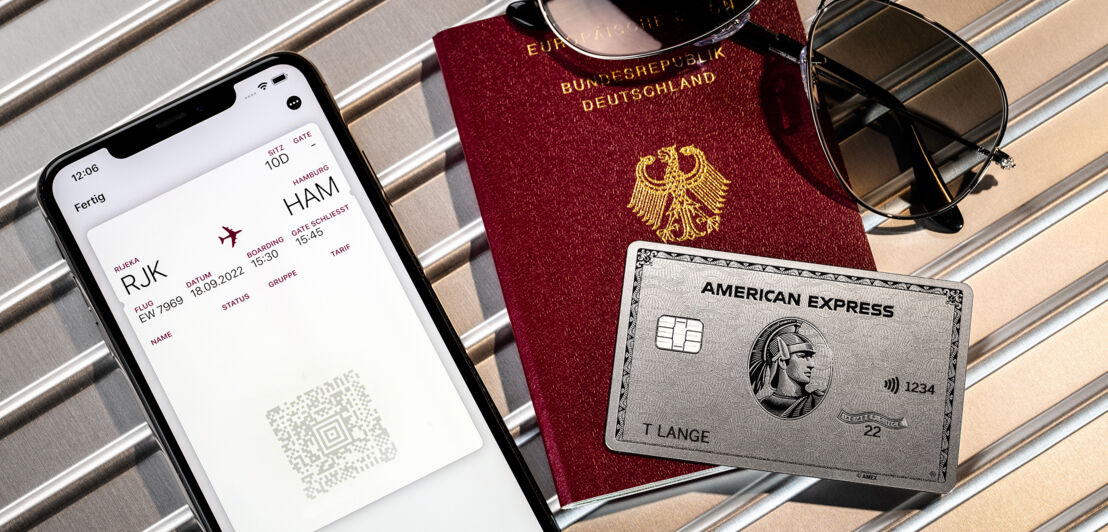 Eine American Express Platinum Card liegt auf einem Reisepass neben einer mobilen Bordkarte auf einem Smartphone.