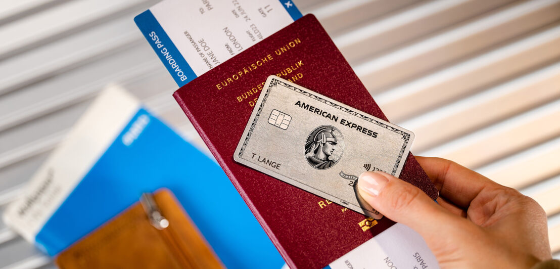 Eine Hand hält eine American Express Platinum Card zusammen mit einem Reisepass und einer Bordkarte.