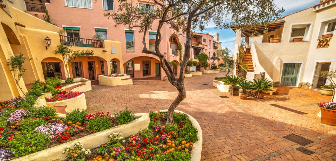 Ein sehr gepflegter Marktplatz auf Sardinien mit pastellfarbenen Häuserfassaden und Blumenbeeten