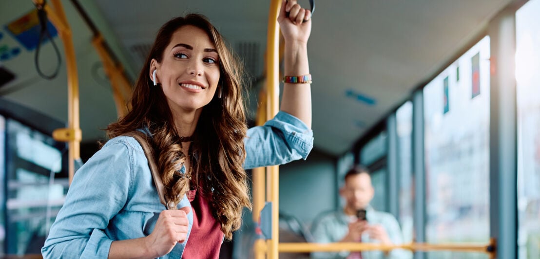 Eine junge Frau hält sich lächelnd in einem Linienbus an einer Halteschlaufe fest.