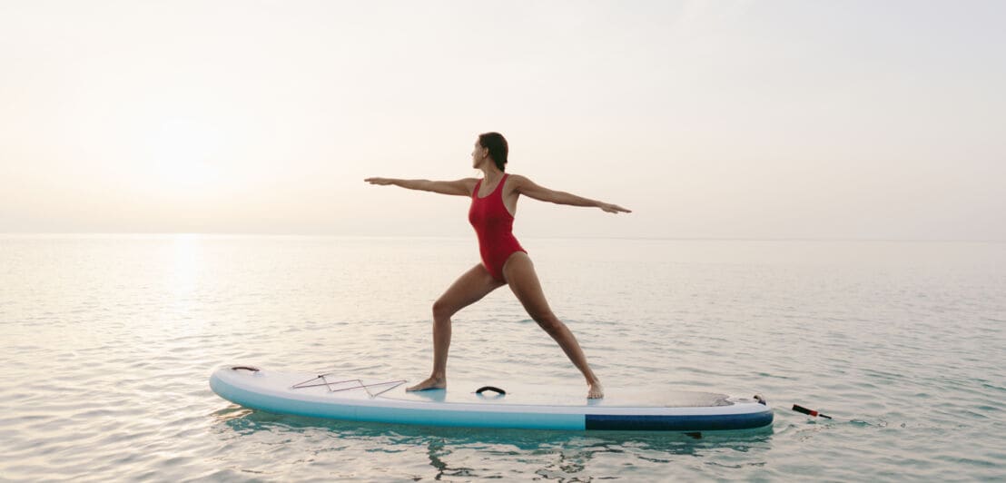 Eine Frau, die auf einem Stand-Up Paddelboard eine Yoga-Übung macht.