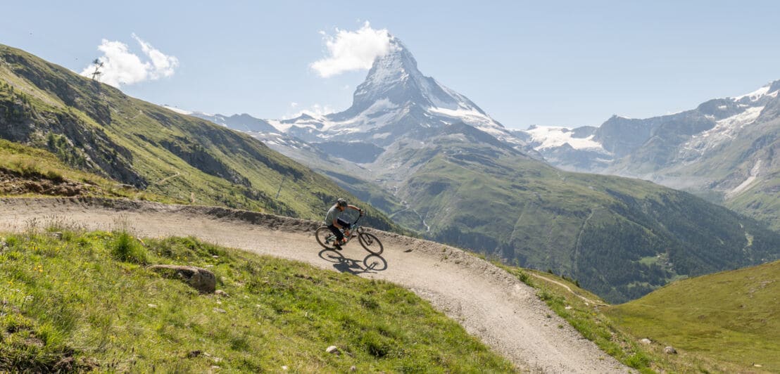 Eine Person mit Mountainbike in den sommerlichen Schweizer Alpen mit Matterhorn im Hintergrund.
