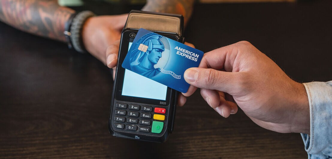 Kontaktlose Zahlung mit einer blauen Kreditkarte von American Express an einem Kartenlesegerät auf einer Theke.