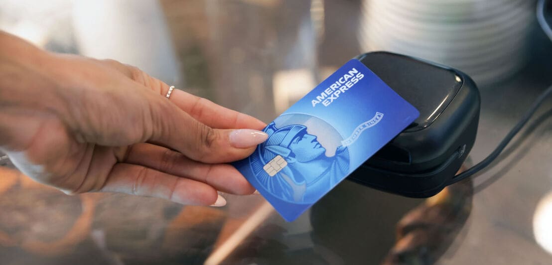 Kontaktlose Zahlung mit einer blauen American Express Kreditkarte an einem Kartenlesegerät.