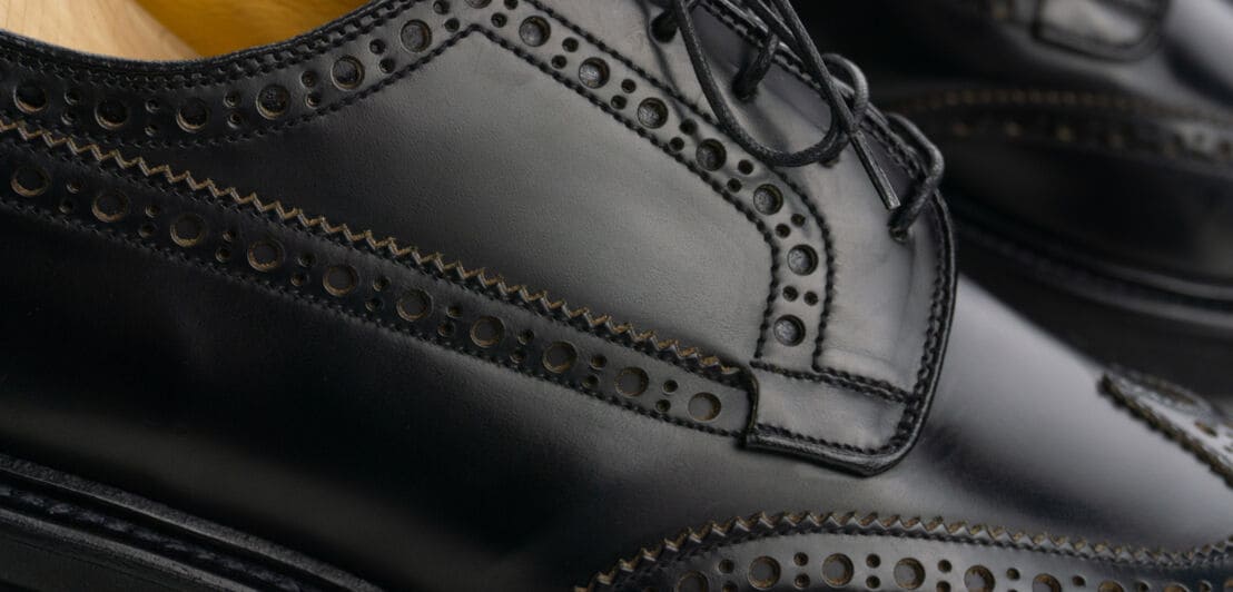 Nahaufnahme eines schwarzen Brogue Derby Schuhs mit Schnürsenkeln, Lochmuster und Derbybogen.