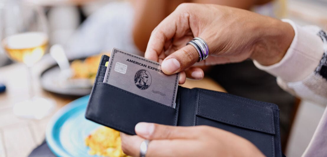 Nahaufnahme einer Hand, die beim Lunch eine silberne American Express Kreditkarte aus einem Portemonnaie zieht.