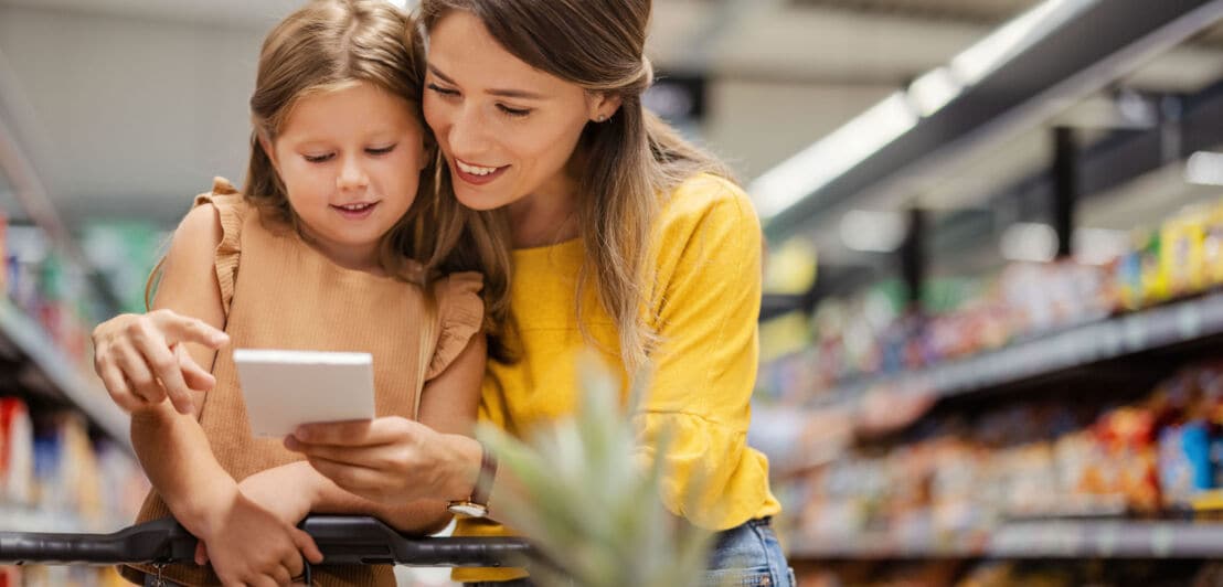 Eine Frau schaut mit ihrer Tochter auf einen Einkaufszettel im Supermarkt.