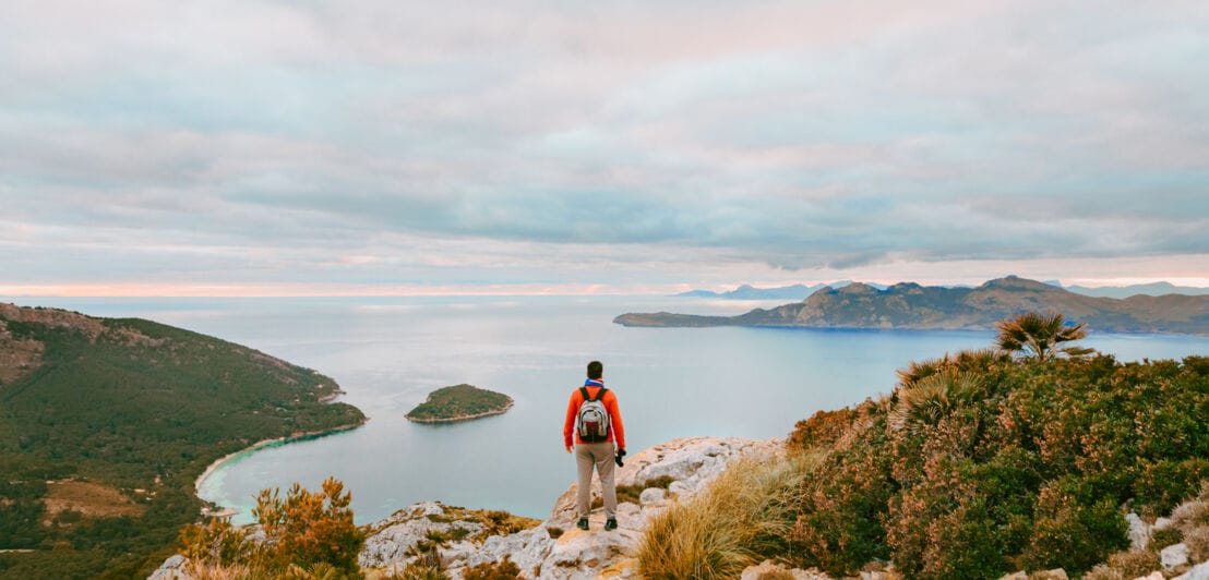 Rückenansicht eines Wanderers auf Mallorca, der an einer Klippe steht und auf das Meer im Hintergrund blickt.