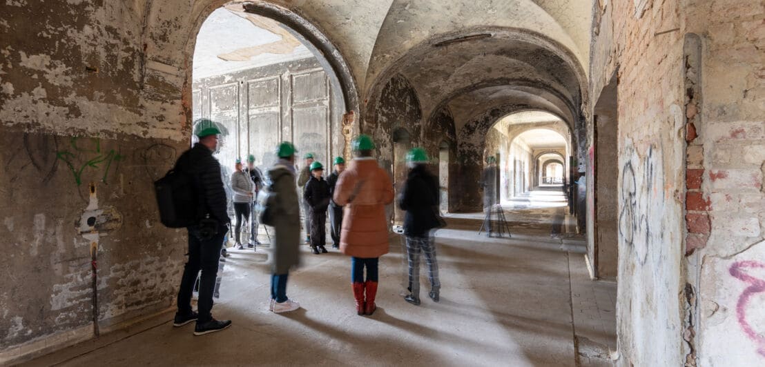 Besuchergruppe mit grünen Bauhelmen in einem alten Gewölbegang.