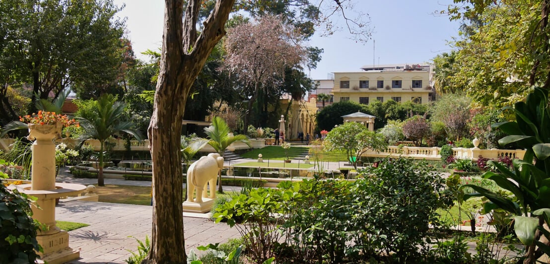 Eine grüne Gartenanlage mit Teich und Elefantenskulptur.