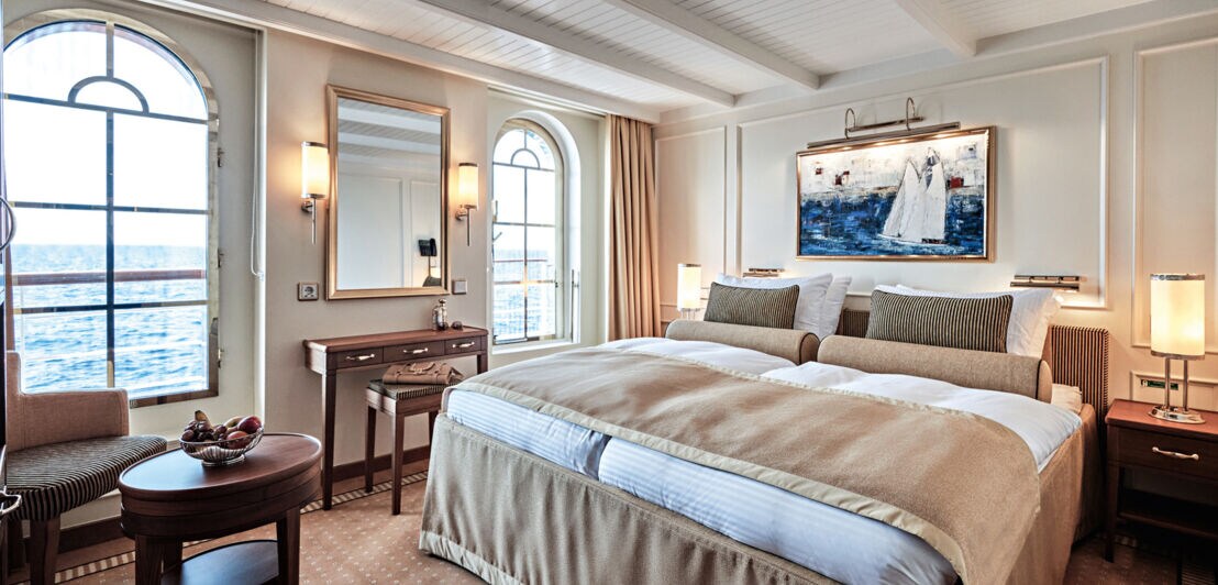 Ein Doppelbett in einer luxuriösen Suite auf einem Schiff mit Blick aufs Meer.