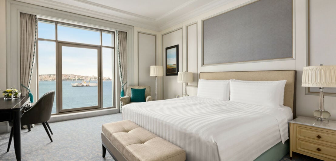 Ein helles Hotelzimmer mit Doppelbett und bodentiefen Fenstern mit Blick auf den Bosporus mit Schiff.