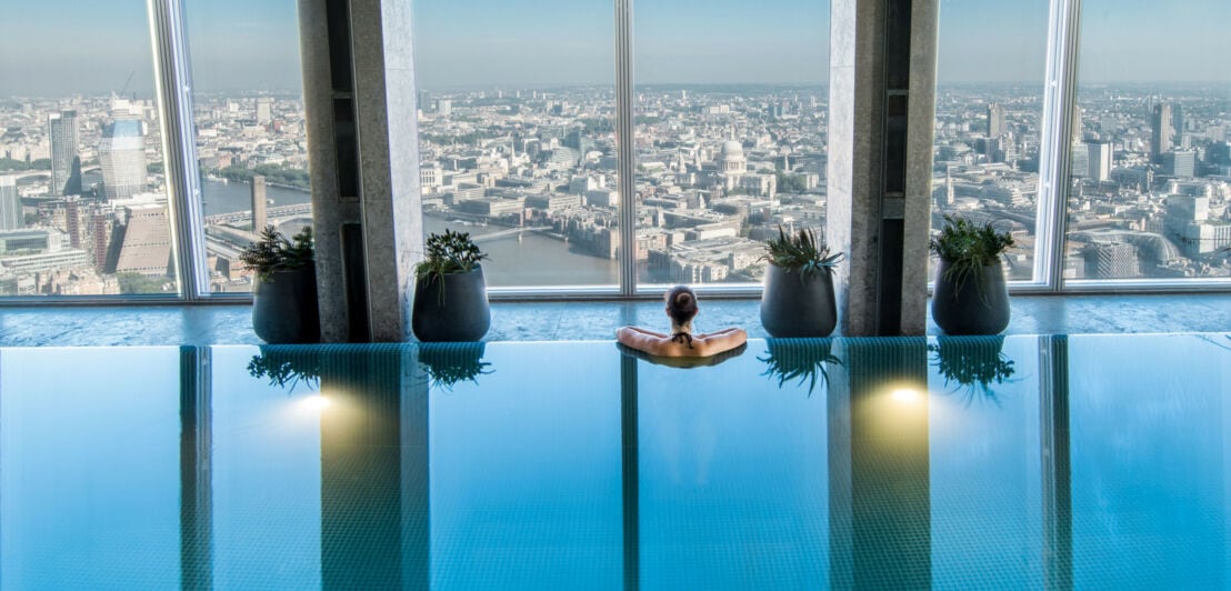 Rückansicht einer Frau in einem Pool im oberen Stockwerk eines Wolkenkratzers mit Ausblick auf die Skyline von London.