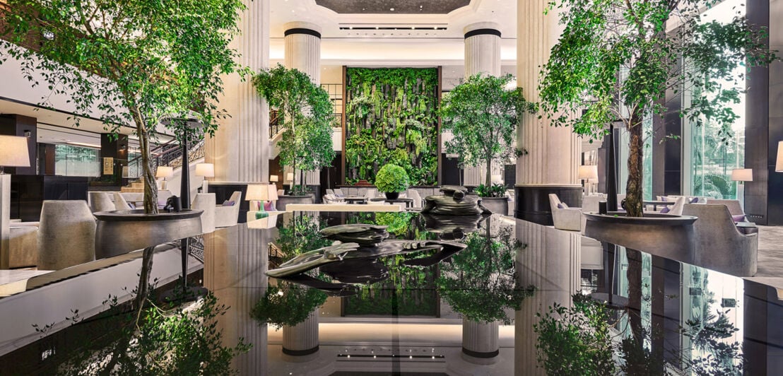 Begrünte Hotelrezeption in einer luxuriösen Empfangshalle mit Marmorsäulen und Bäumen.