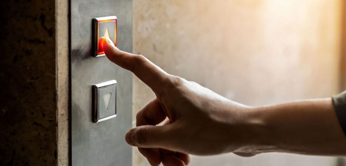 Eine Person drückt mit dem Zeigefinger auf einen Aufzugsknopf.