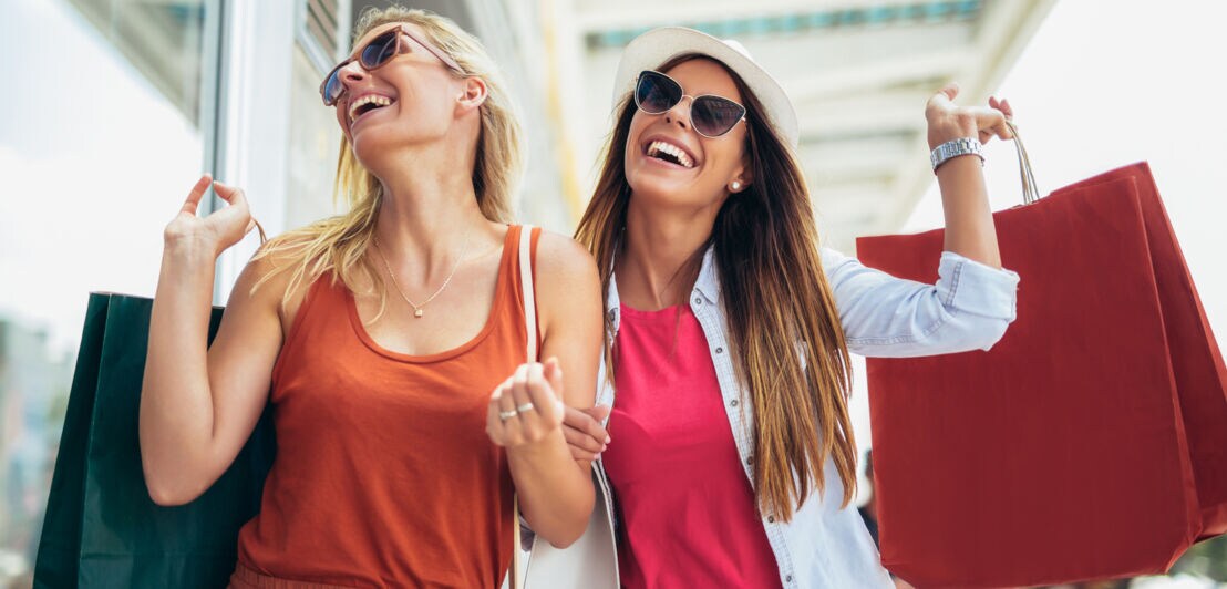 Zwei lachende Frauen in sommerlicher Kleidung mit Einkaufstüten.