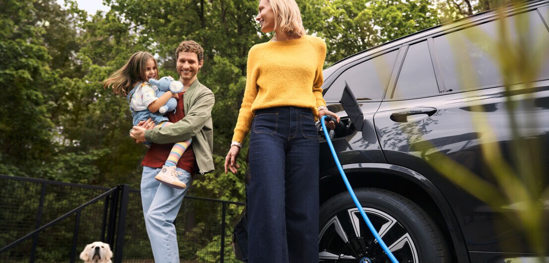 Eine glückliche Familie mit Kind und Hund beim Laden eines BMW-Elektroautos.