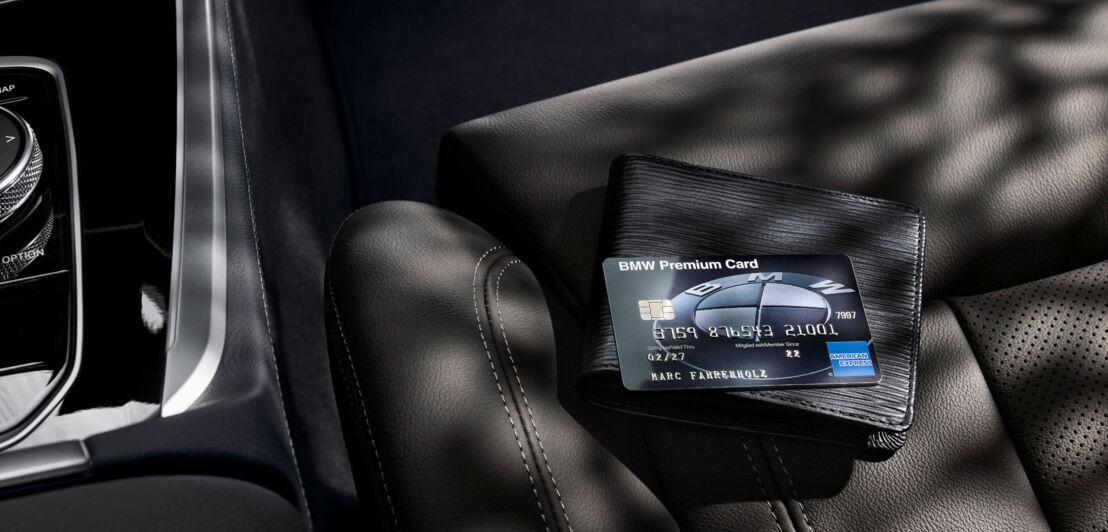 Eine schwarze BMW Premium Card liegt auf einem Schwarzen Portemonnaie auf einem schwarzen Autositz aus Leder.