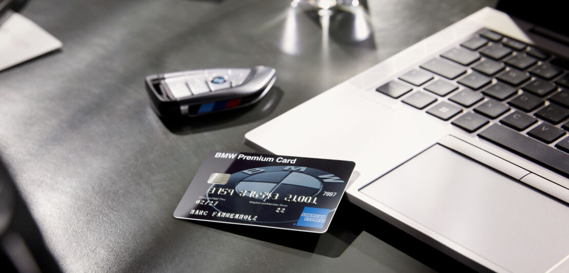 Eine BMW Premium Kreditkarte liegt auf einem Schreibtisch auf einem Laptop neben einem BMW Autoschlüssel.