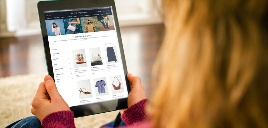 Eine Person hält ein Tablet mit Modeartikeln des Onlineshops NET-A-PORTER auf dem Display in den Händen.