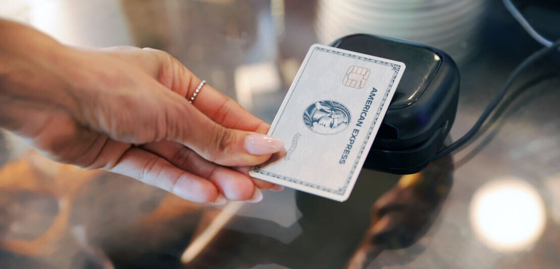 Kontaktlose Zahlung mit einer silbernen Kreditkarte von American Express an einem Kartenlesegerät.