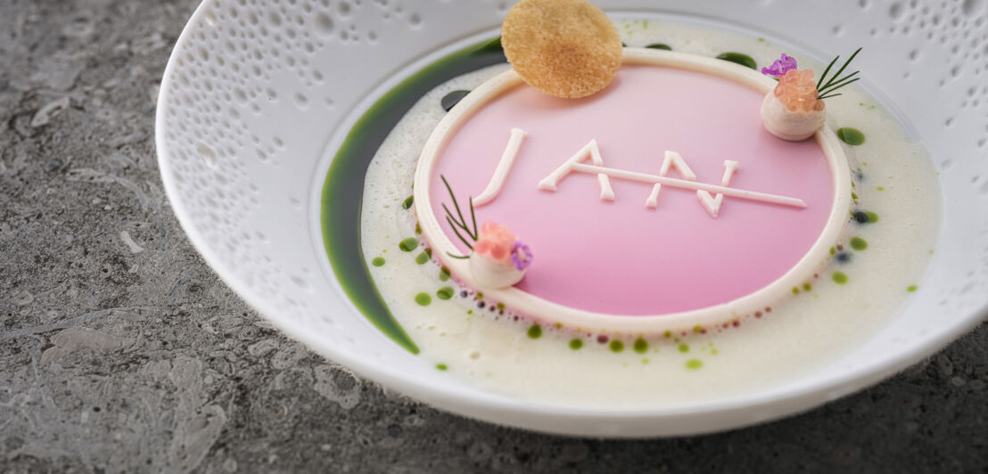 Eine kunstvoll angerichtete Speise in Pastelltönen mit dem Schriftzug JAN auf einem weißen Teller.