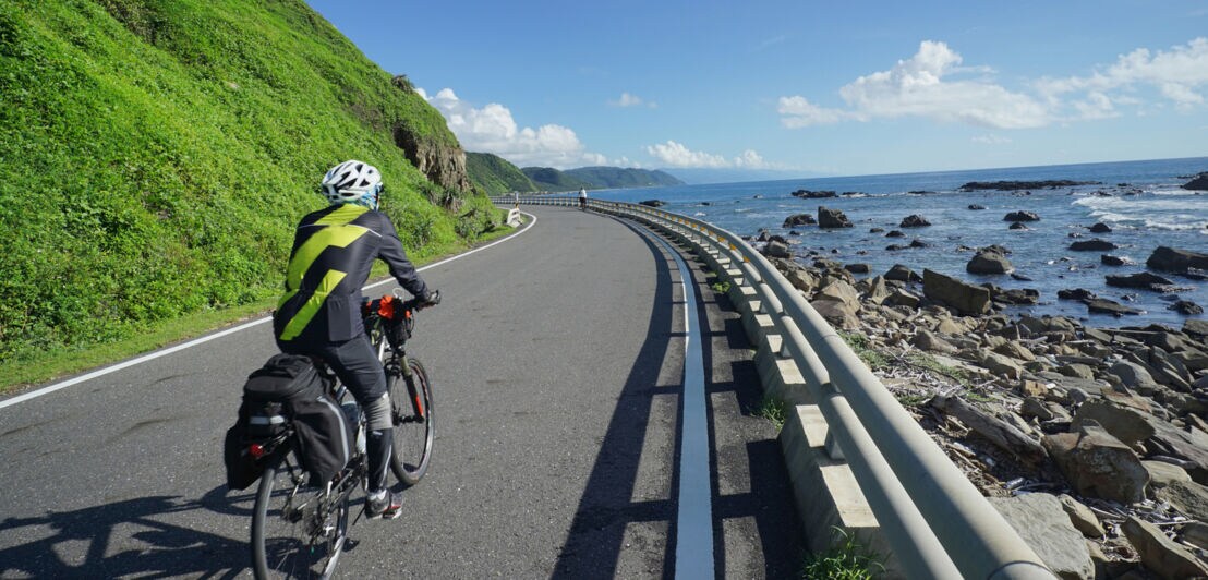 Rückansicht eines fahrenden Mountainbikers auf einer Küstenstraße.