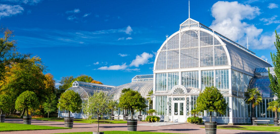 Parkanlage in Göteborg mit weißem Gewächsaus, vor dem ein paar Sträucher in großen Pflanztöpfen arrangiert sind.