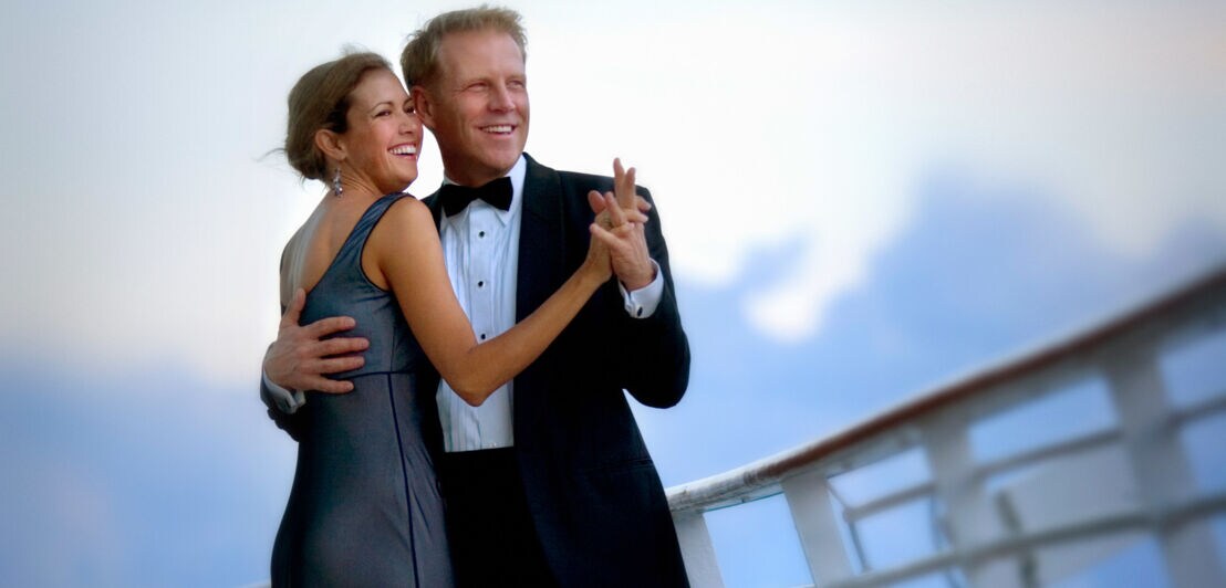 Ein tanzendes Paar in Abendgarderobe auf dem Außendeck eines Schiffes.