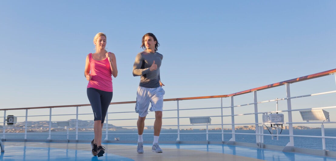 Ein Paar in Sportkleidung läuft auf dem Deck eines Kreuzfahrtschiffes auf See.