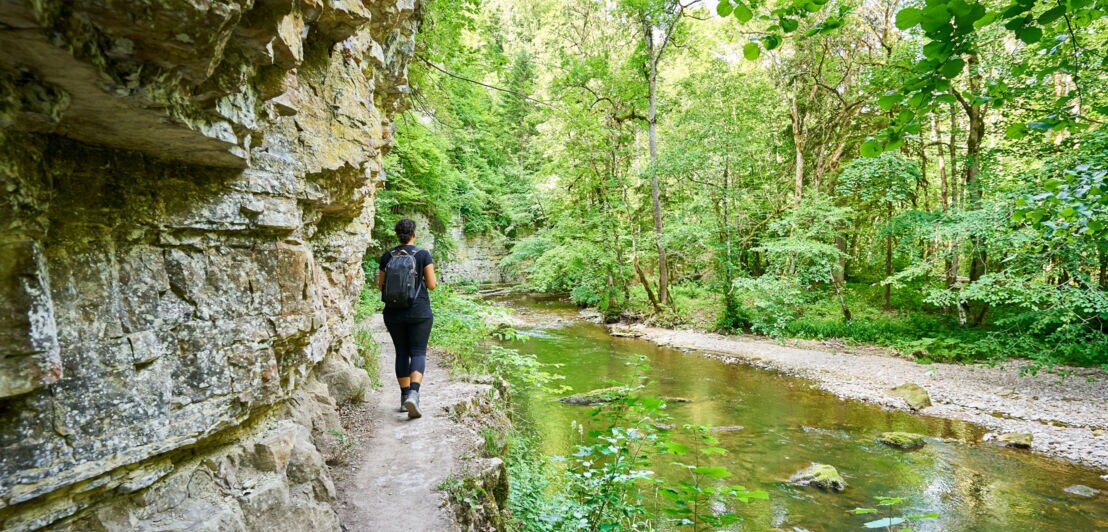 Eine Person wandert in der Wutachschlucht, entlang schroffer Felswänden und einem idyllischen Bachlauf.
