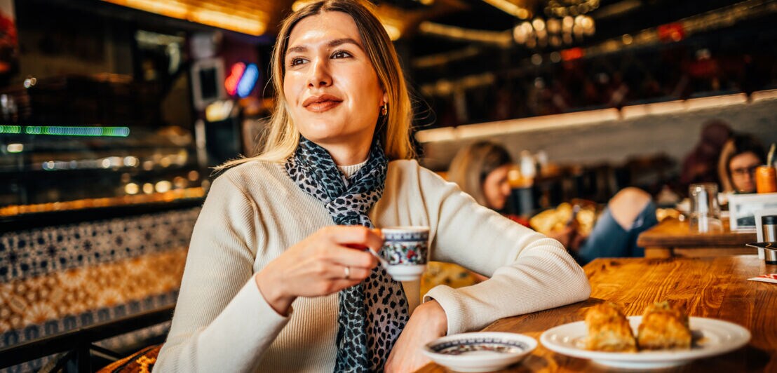 Eine Frau sitzt mit einem türkischen Mokka und Gebäck in einem Café.