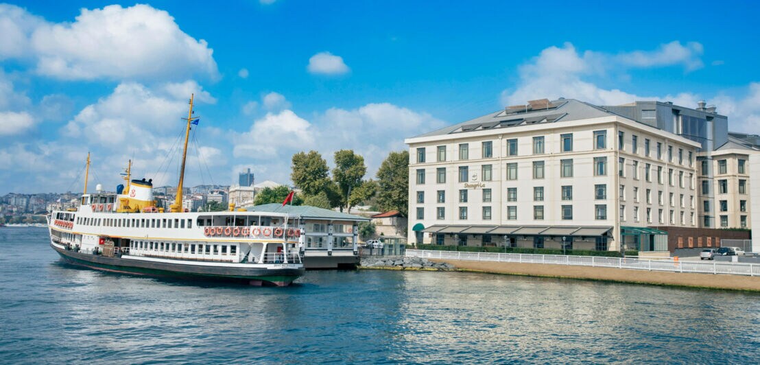 Ein Schiff vor einem weißen Hotelgebäude am Wasser in Istanbul.