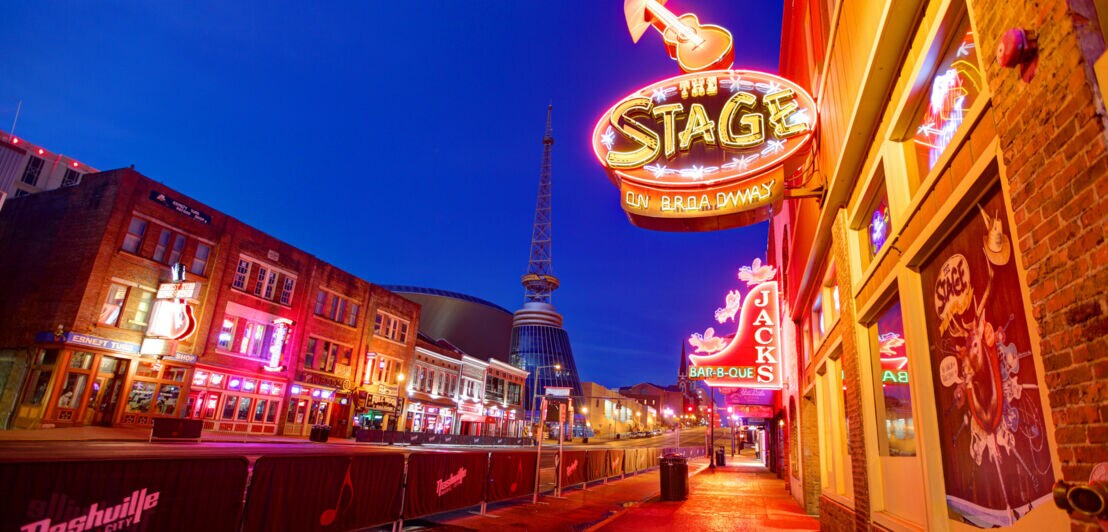 Eine Straße mit beleuchten Bars und Musikclubs bei Nacht.