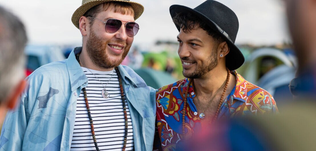 Zwei Männer mit Hüten und in bunter Kleidung auf einem Festival.