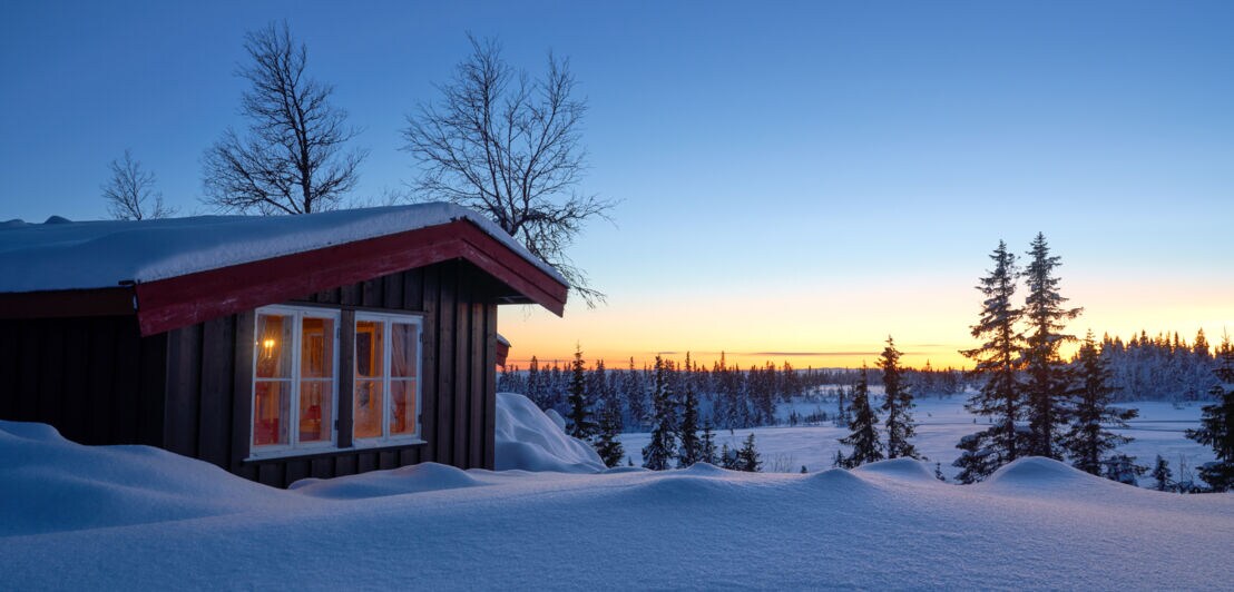 Hütte bei Sonnenuntergang in einer verschneiten Landschaft.