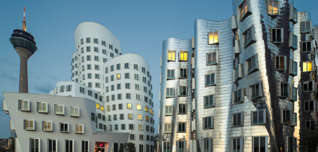 Mehrere moderne, organisch geformte Gebäude, dahinter ein Fernsehturm.