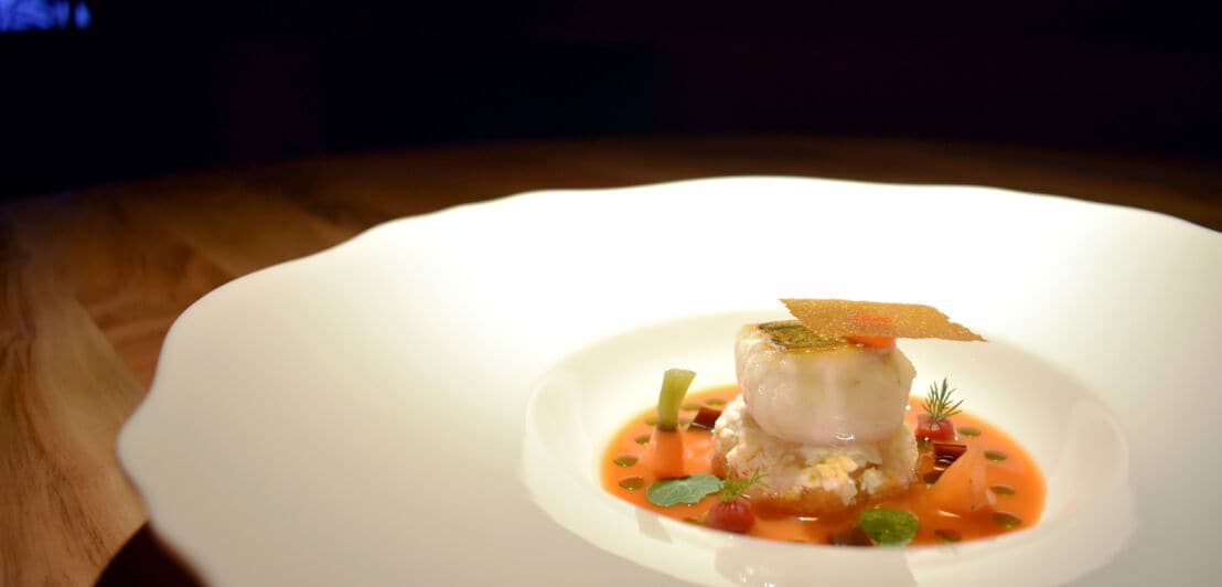 Ein Fischgericht, edel angerichtet auf einem großen weißen Teller.