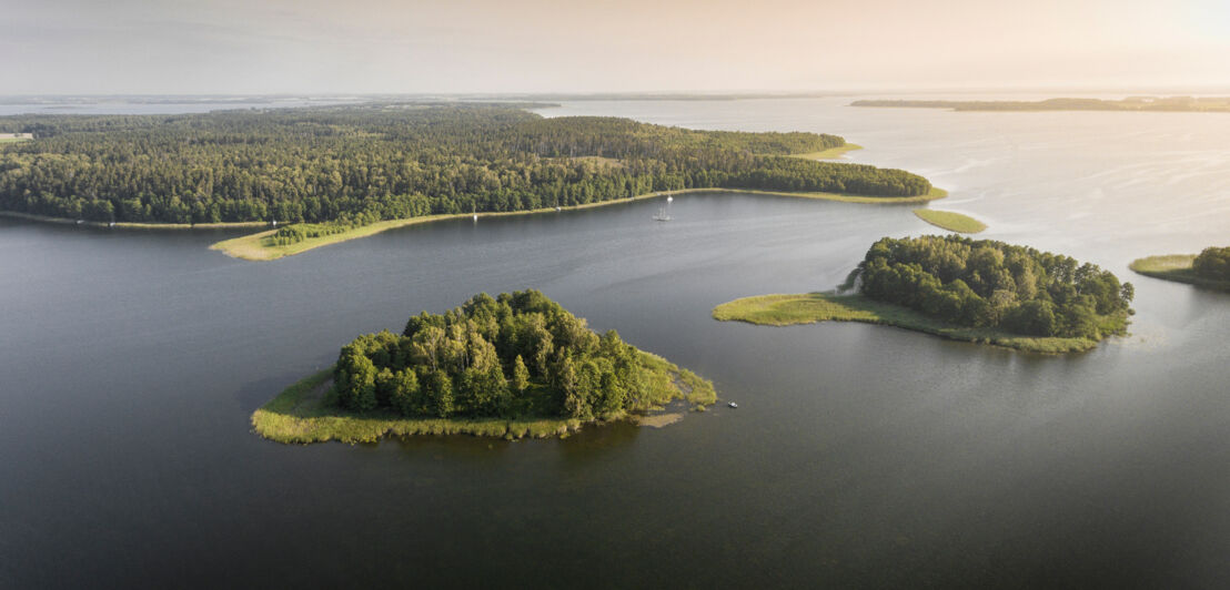 Luftaufnahme mit kleinen grünen Inseln im ruhigen Wasser der Masurischen Seenplatte.