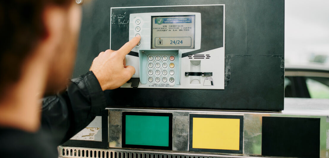 Nahaufnahme eines Mannes, der das Display eines Tankautomaten bedient.