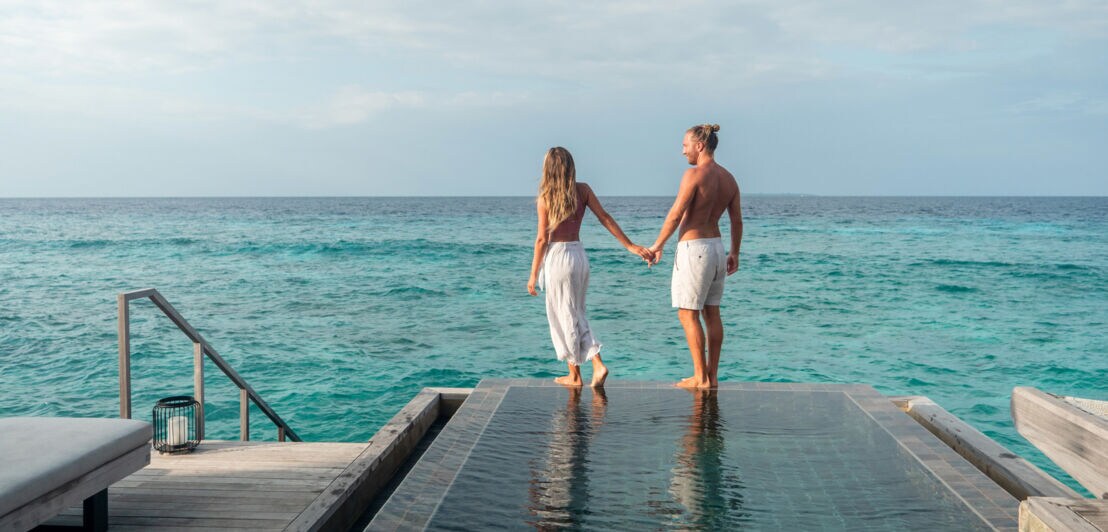 Rückansicht eines Paares in Sommerkleidung an einem luxuriösen Pool am Meer.