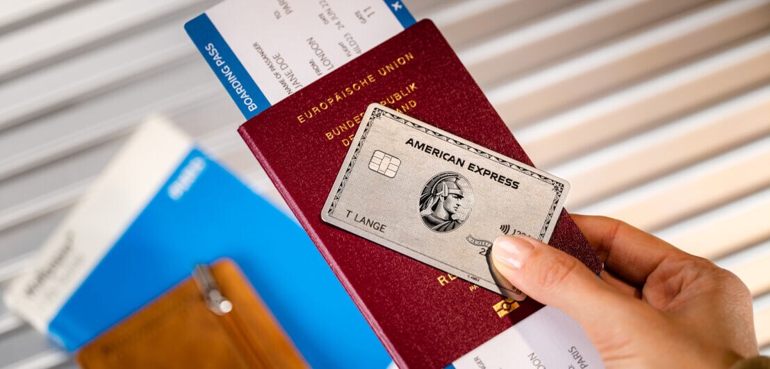 Eine silberne Platinum-Kreditkarte von American Express auf einem Reisepass mit Bordkarte, gehalten in einer Hand.