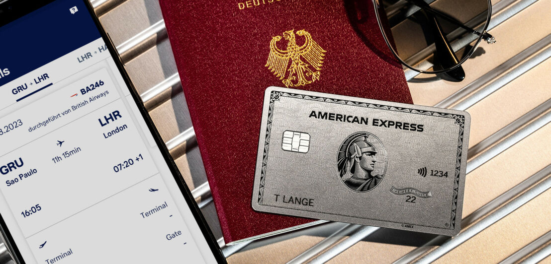 Eine silberne Platinum Kreditkarte von American Express auf einem Reisepass neben einem Smartphone mit Bordkarte auf dem Display.