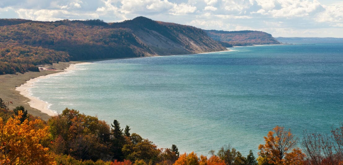 Blick auf die Küste des Michigansees am Ufer des Naturreservats Green Point Dunes mit herbstlich bunten Bäumen.