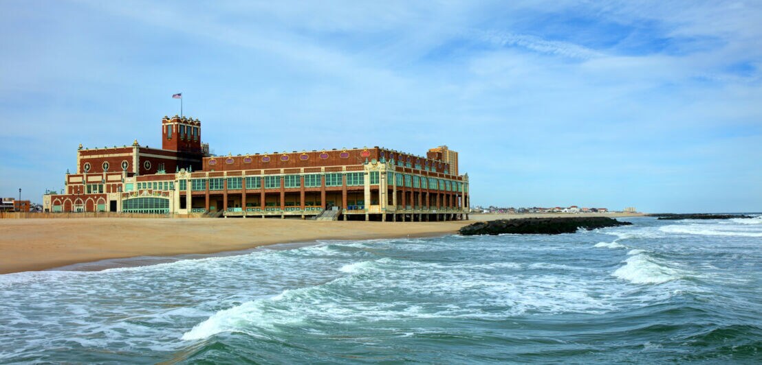 Blick vom Wasser auf ein großes Gebäude mit US-Flagge an einem Sandstrand.