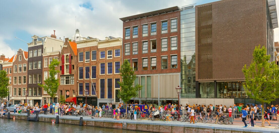 Viele Personen auf einer Promenade an einem Kanal vor dem Museum des Anne-Frank-Hauses.