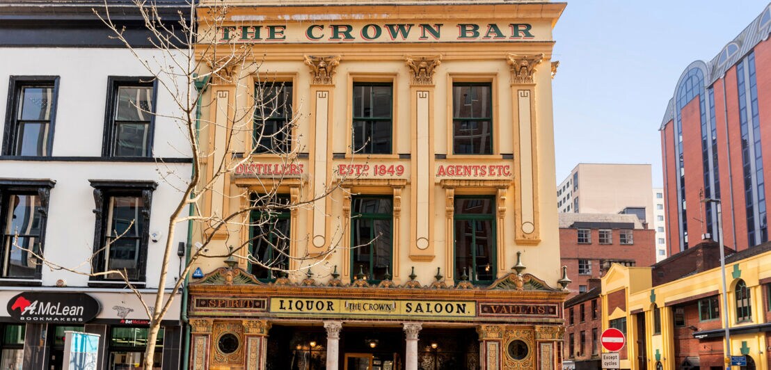 Fassade der historischen Kneipe 'The Crown Bar' mit goldener Verzierung und Schildern wie 'Liquor Saloon' in einer Stadtstraße