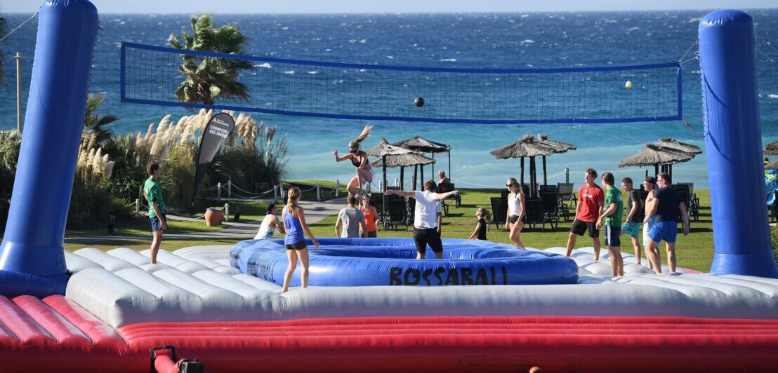 Personen beim Ballspiel an einem Volleyballnetz auf einer Hüpfburg am Meer.